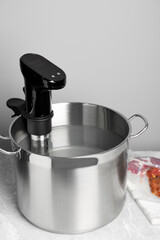 Thermal immersion circulator in pot and vacuum packing with meat on light grey table. Sous vide...