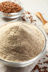 Glass bowl of buckwheat flour and cloth on white table, closeup