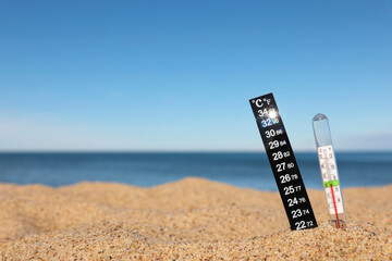 Weather thermometers in sand near sea, space for text