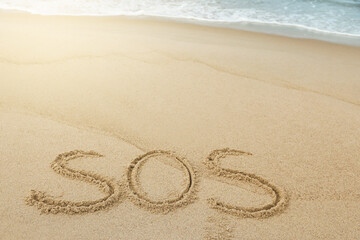 Fototapeta na wymiar Message SOS drawn on sand near sea