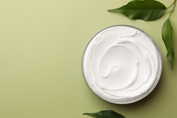 Jar of face cream and fresh leaves on light green background, flat lay. Space for text