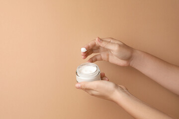 Woman applying face cream on beige background, closeup. Space for text
