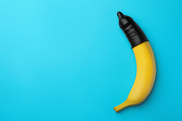 Banana with condom on light blue background, top view and space for text. Safe sex concept