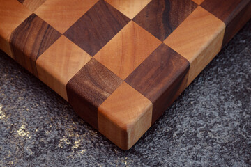 End cutting board on a dark textured background. Kitchen utensils made of natural wood. Expensive vintage items. Luxurious quality woodworking. Chess pattern on a wooden board.