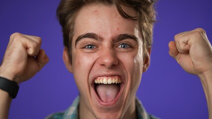 Closeup of excited jubilant overjoyed young man 20s doing winner gesture celebrate clenching fists say yes isolated on purple background studio portrait