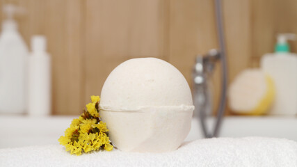 Towel with bath bomb and flowers on tub indoors, closeup
