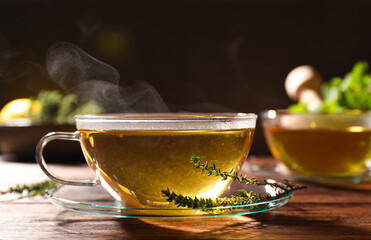 Cup of aromatic herbal tea and fresh thyme on wooden table