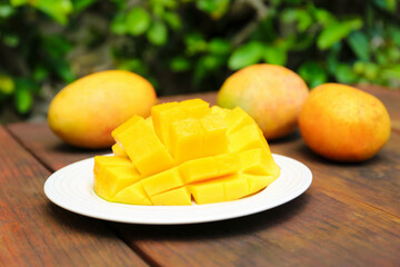 Delicious ripe cut and whole mangos on wooden table outdoors