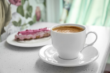 Cup of delicious aromatic coffee and eclair on white table indoors, closeup