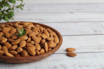 Plate with tasty almonds on white wooden table. Space for text