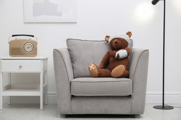 Toy bear with bandages sitting in armchair indoors