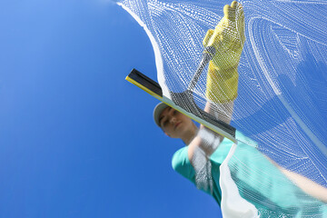 Woman cleaning glass with squeegee on sunny day