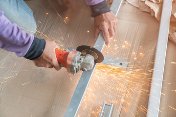 Worker cutting metal with electric grinder.