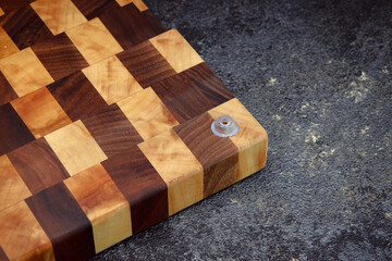 End cutting board on a dark textured background. Kitchen utensils made of natural wood. Expensive vintage items. Luxurious quality woodworking. Chess pattern on a wooden board.