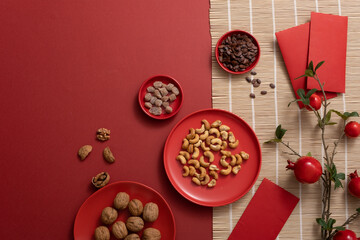 Traditional food for Chinese new year background. Plates of nuts, pomegranate branches, lucky envelopes, and bamboo blinds on a red background. Empty space