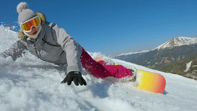 CLOSE UP: Young woman is learning to ride snowboard when she drops down on snow. Female beginner snowboarder crashes towards camera while making snowboard turn on slope at snowy mountain ski resort.