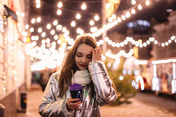 Thoughtful young woman walking in city street during Christmas holidays at night