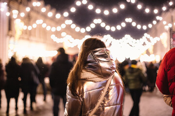 Back view of young woman walking in city street during Christmas holidays at night
