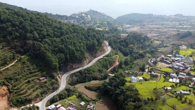 A beautiful aerial view of the Himalayan Foothills with a road winding along the base of a hill with scattered fields and houses.