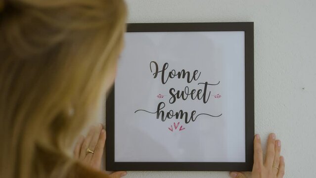 Woman hanging up "home sweet home" frame on wall.