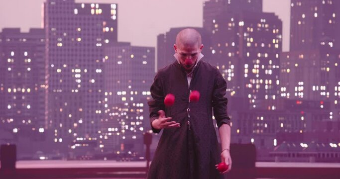 Mime or clown juggling red balls in the background of the modern city skyline at night.