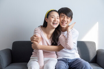 Laughing and hugging asian brother and sister with care and love on sofa at home.