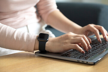 Fototapeta premium Hands of woman wearing smartwatch and working on the keyboard of her laptop computer.