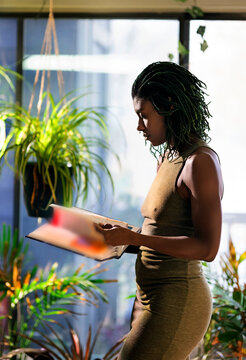 Black woman with green dreadlocks  wearing green dress standing in the living room, reading book