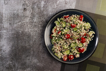 Couscous salad with Cucumbers, Tomatoes and Pink Onions on a round plate on a dark background. Top view, flat lay