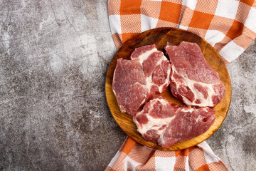 Raw fresh pork neck meat steaks on a round wooden cutting board on a dark grey background. Top view, flat lay