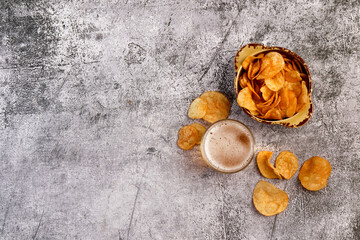 Сold beer in a glass and potato chips in a bowl on a dark grey background. Top view, flat lay