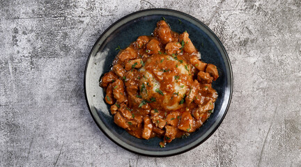 Tomato Pork stew with rice on a round plate on a dark gray background. Top view, flat lay.