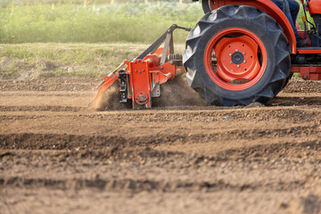 Tractor cultivating land with a rotary tiller in farm.