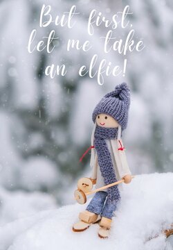 But first, let me take an elfie Inspiration joke quote phrase Angel gnome in scarf and knitted hat skiing on snowy fir branch Elf toy on skis in snowy landscape New year and Merry Christmas greeting