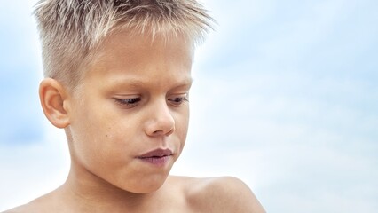Boy with blue lips frozen from swimming in cold water at sea resort. Blond junior schoolboy gets...