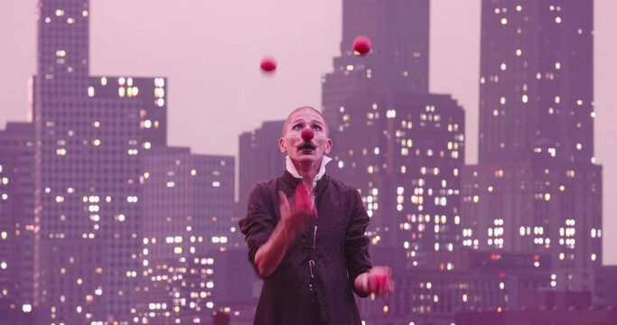 Mime or clown juggling red balls in the background of the modern city skyline at night.