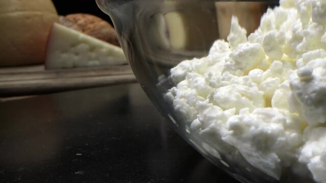 Snow-white cottage cheese in a transparent salad bowl and cheese on the table.