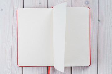 Red diary book with white empty papers, turn from right to left on white wooden background. Start living from scratch, new beginning. Personal organizer as reminder, making notes. Top view, copy space