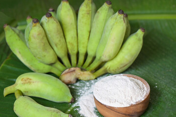 banana powder on wooden bowl and raw banana - banana fruit on leaf background, alternative flour,...
