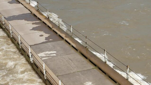 Muddy flood water in fast river current almost overflows narrow bridge