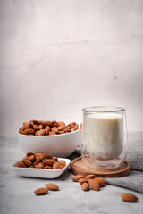 Glass of almond milk with almond seed on white concrete background.