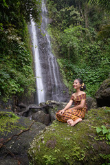 Fototapeta na wymiar Portrait of two girl in front of a waterfall in a tropical forest, dressed in a traditional sarong