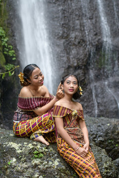 Portrait of two girls in front of a waterfall in a tropical forest, dressed in a traditional sarong