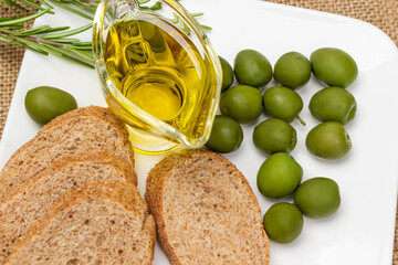 Green olives, bowl of olive oil and baguette pieces on white plate. - Powered by Adobe