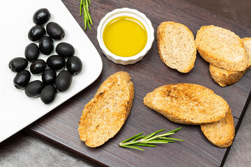 Black olives on a white plate. Toast and olive oil in a bowl.