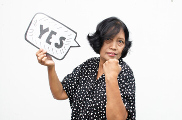 Portrait of happy ecstatic senior asian woman making yes winning gesture with raising her fist while holding yes bubble sticker isolated over white