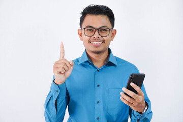 smiling employee asian man with glasses holding phone with finger pointing up wearing blue shirt isolated white background