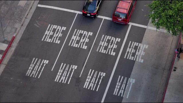 Top view on the passing cars on the road. Cars riding on the street sign. Wait here sign. Colourfull cars Drive throught the avenue in Los Angeles. Big city life, LA day. slow motion 4k