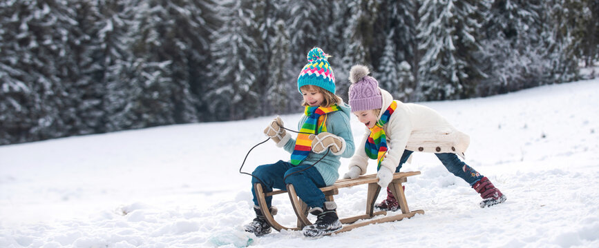 Funny children in snow ride on sled. Winter outdoors games. Happy Christmas family vacation concept. Kids enjoy the holiday.
