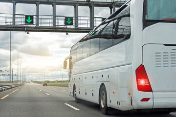 White modern comfortable tourist bus driving through highway at bright sunny day. Travel and coach tourism concept. Trip journey by vehicle. Green glowing arrows point to an open road ahead.